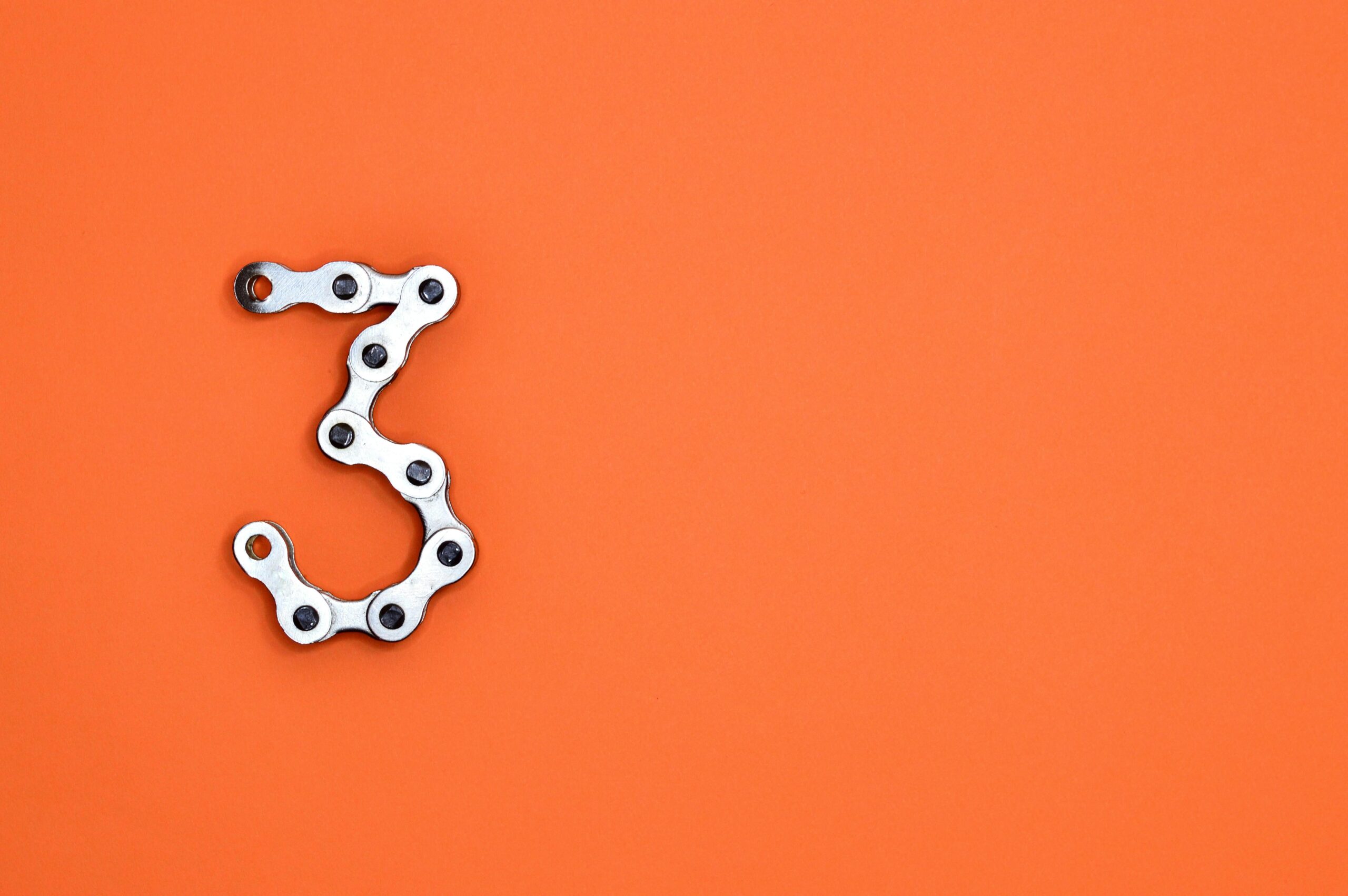 A bicycle chain forms the number three against a vibrant orange backdrop, offering ample copyspace.